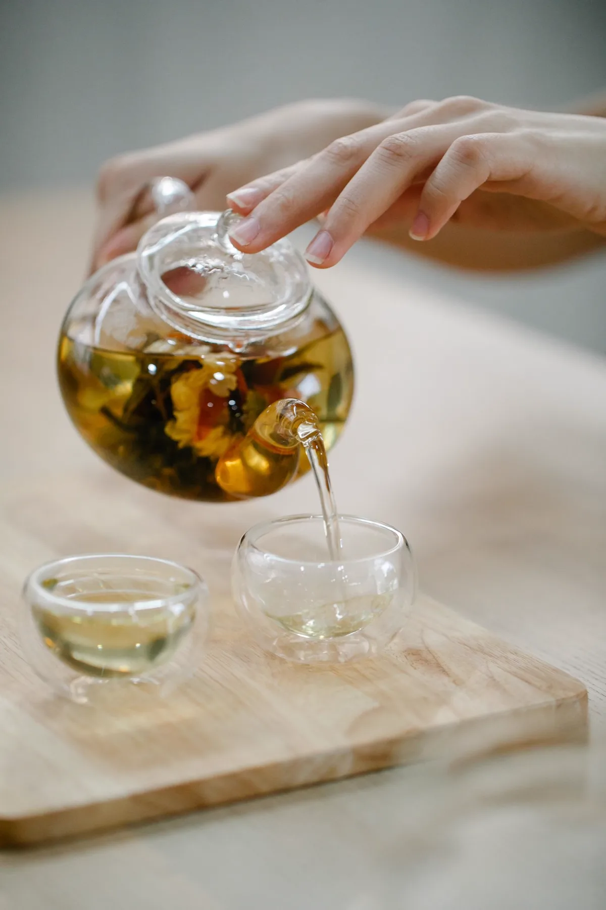 Whole green tea leaves unfurling in a glass teapot as the tea is poured into a small glass cup