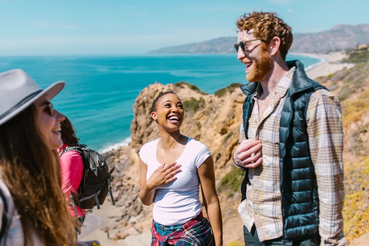 Two people laughing together on a coastal walking path with the sea behind them