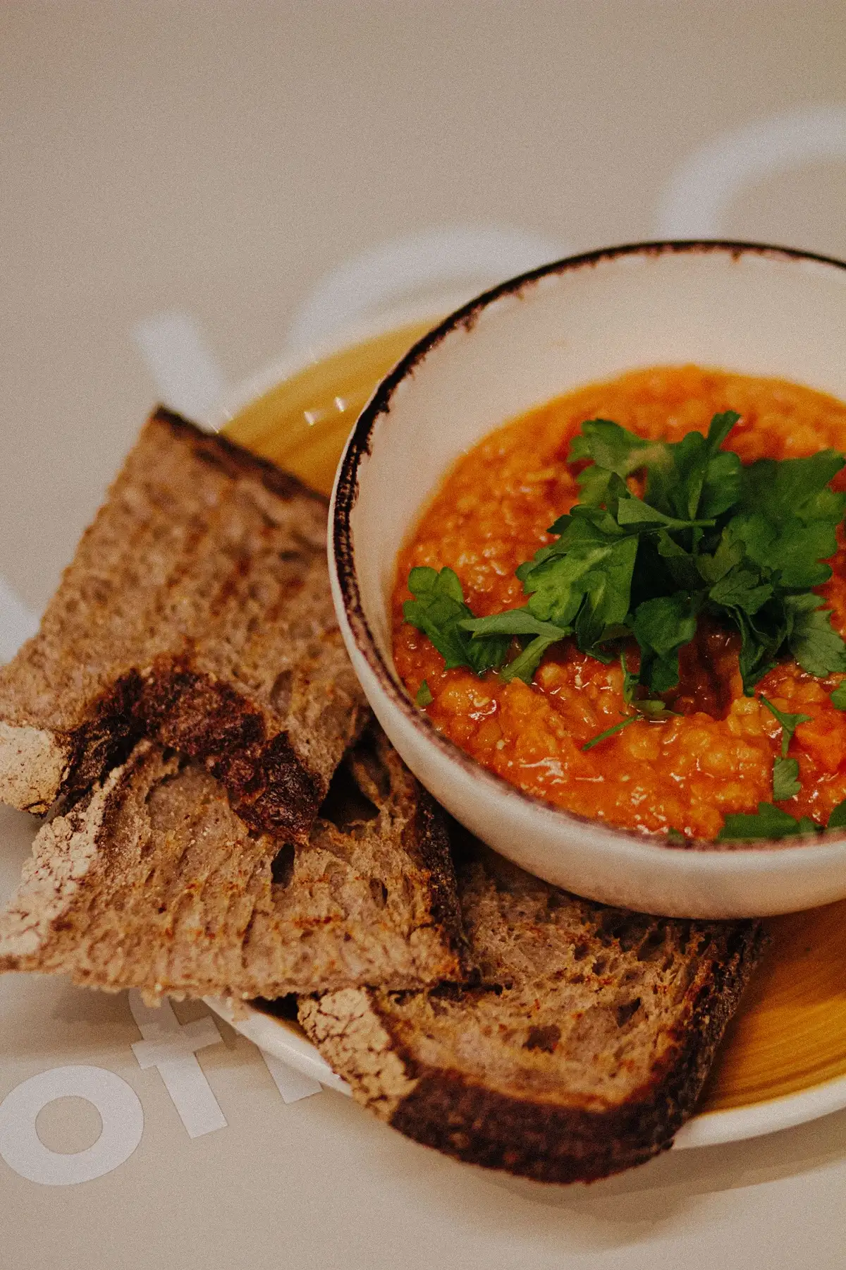 A pot of lentil soup garnished with fresh parsley, beside slices of rustic bread