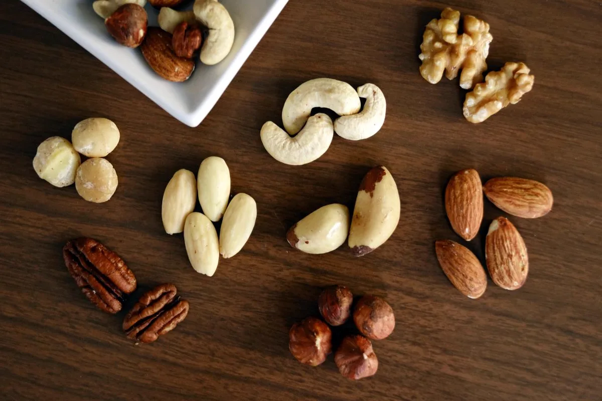 An assortment of nuts including pale shelled Brazil nuts on a dark wooden board
