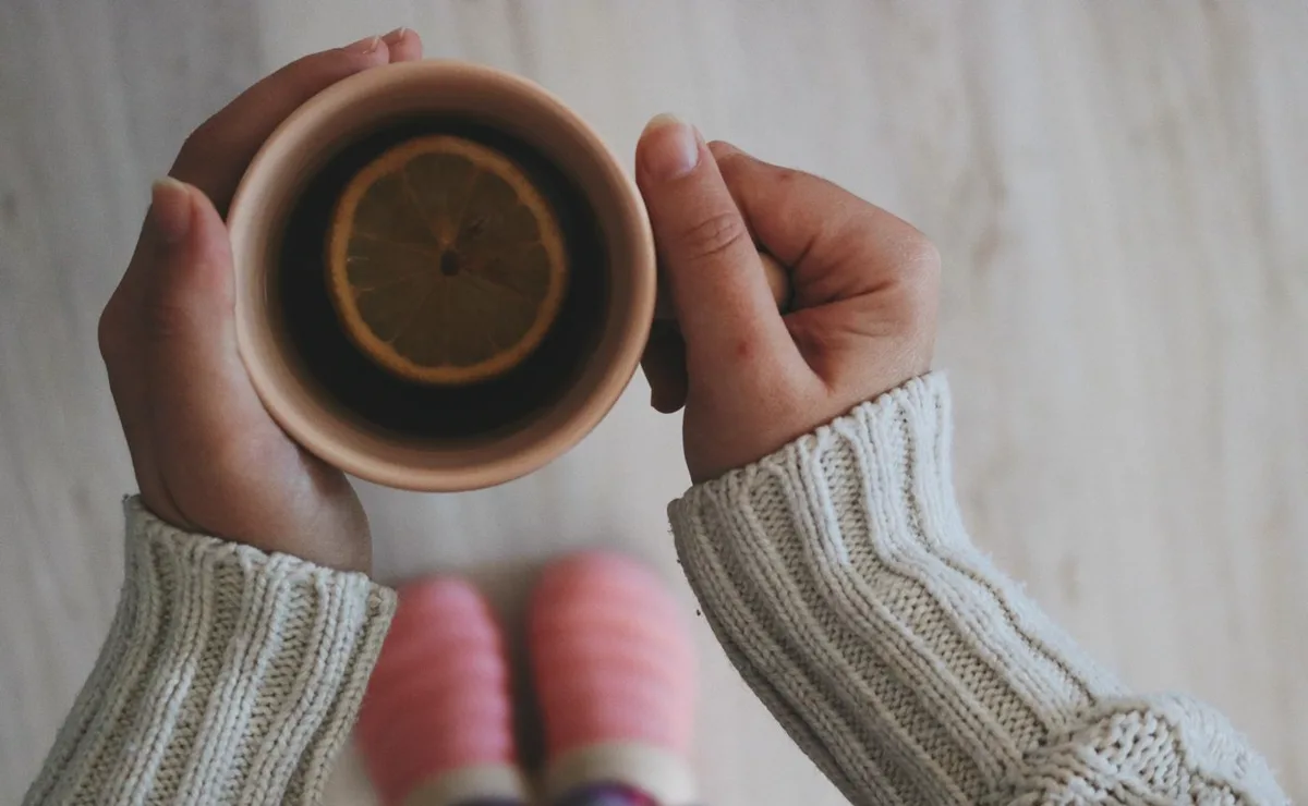 Two hands cradling a warm mug of tea with a slice of lemon floating on top