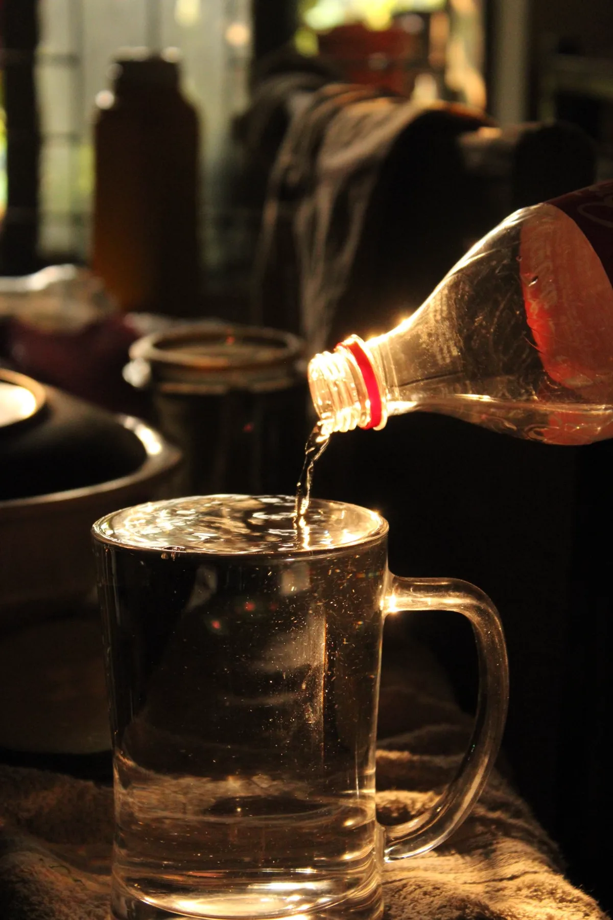 Water being poured from a bottle into a clear glass mug in warm low light